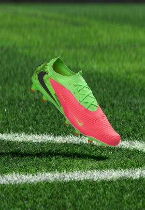 Lys grønn og rosa fotballsko svever i luften over en hvit linje på en gressbane med svarte og oransje knotter.