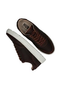 Bruine leren sneakers met een witte rubberen zool, ronde neus en geperforeerde details. Bruine veters passen bij het ontwerp van de bovenkant. Merkenlogo zichtbaar aan de binnenkant.