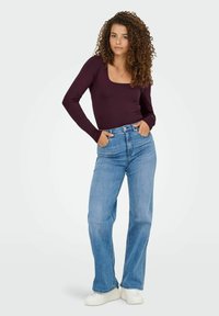 Top a maniche lunghe bordeaux abbinato a jeans a vita alta blu chiaro a gamba larga e scarpe da ginnastica bianche, con tasche e design aderente.