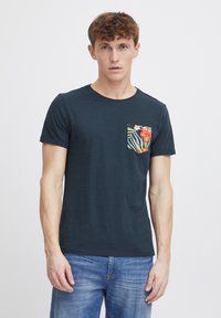 Camiseta de manga corta azul marino hecha de algodón, con un bolsillo estampado de diseño floral y rayas. Cuello redondo estándar y corte relajado.