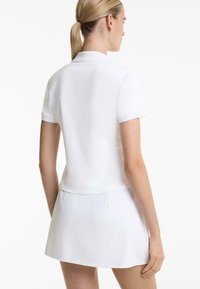 White polo dress featuring a fitted bodice, short sleeves, and a flared skirt. Made from smooth, stretchable fabric with a classic collar.