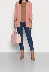 Lichtroze blazer over een bruin gebreid trui, blauwe denim jeans en tan kleurige enkellaarsjes met hak; met een roze handtas.