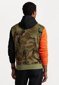 Bluza z kapturem z kamuflażowym wzorem w zielonym i brązowym kolorze, z czarnymi i pomarańczowymi rękawami oraz zielonym, prążkowanym ściągaczem.
