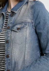 Denimjacka i ljusblå med en urtvättad look, med knäppning framtill, två bröstfickor och krage.