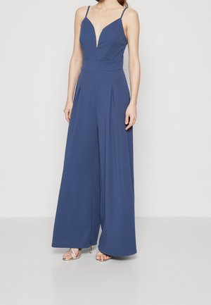 Marineblå jumpsuit med dyb V-hals, tynde stropper, tætsiddende talje og vide ben med plisseringer. Glat stof med minimal tekstur.
