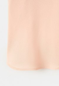 Light peach fabric with a smooth texture and slightly curved hem, showing detailed stitching along the edge.