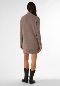 Strickkleid in sanftem Taupe, mit hohem Kragen und geripptem Saum; kombiniert mit schwarzen westernstil Stiefeln.
