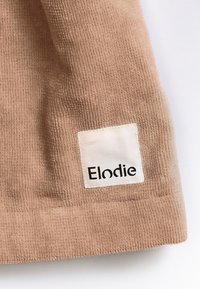 Ljusbrun kordflorsduk med en slät yta, försedd med en rektangulär vit etikett med texten "Elodie" i svart.