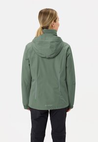 Giacca impermeabile verde con cappuccio, caratterizzata da una linea dritta, zip laterali e dettagli riflettenti. Il tessuto è liscio e leggero.