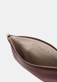 Borsa in pelle bordeaux con zip dorata, interno in tessuto beige e etichetta cucita con la scritta "Coccinelle pelle italiana autentica."