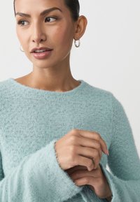 Mintgrüner, weicher, flauschiger Strickpullover mit weitem Ausschnitt und langen Ärmeln. Verfügt über eine strukturierte Oberfläche und leicht ausgefranste Bündchen.