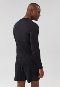 Black long-sleeve athletic shirt with a fitted design, smooth texture, and a crew neckline, paired with black shorts.