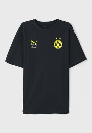Musta puuvillapaita keltaisilla graafikoilla. Sisältää Puma-logon, "KidSuper Studios" tekstin ja "BVB 09" embleemin, jossa on kaksi tähteä. Lyhythihainen.