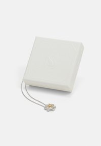 Silver necklace with floral pendant featuring clear gemstones and a gold accent, displayed alongside a textured white box.