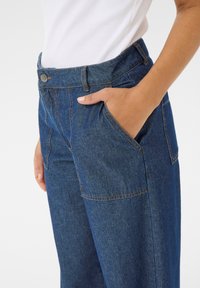 Pantalons en denim bleu foncé avec taille haute, jambes droites, poches latérales, coutures contrastantes et fermeture à bouton à l'avant.