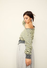 Gestreifter Pullover in Gelb und Grau mit schulterfreiem Design und grauem Rippbund. Kombiniert mit hellgrauen Hosen mit glatter Textur.