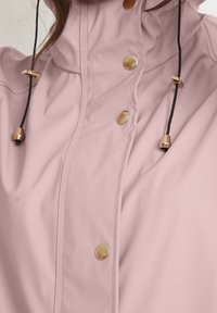 Lichtroze jas met gouden drukknopen en zwarte trekkoorden met gouden metalen uiteinden, gedragen door een persoon.