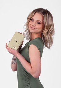 Light green wallet with a smooth texture, featuring a snap closure and small white dots, held in one hand against a neutral background.