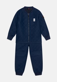 Marineblauer gesteppter Trainingsanzug mit Reißverschlussjacke und elastischen Bündchen; er zeichnet sich durch Rautenmuster und strukturierte Akzente an Ärmeln und Hosen aus.
