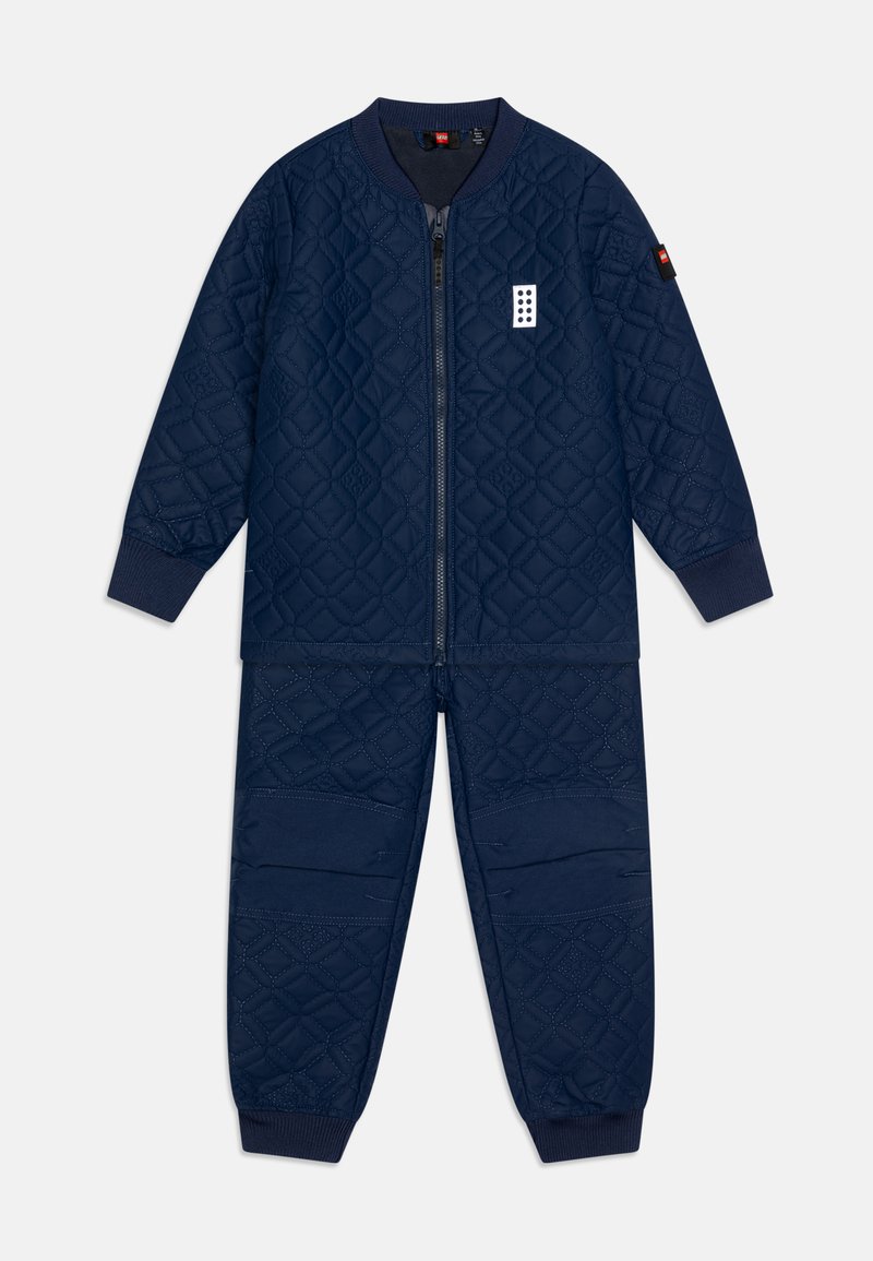 Tamsiai mėlyna užsegama treniruotė su pūkine striuke ir elastingomis Rankovėmis; savybės: deimanto raštai ir tekstūruoti akcentai ant rankovių ir kelnių.