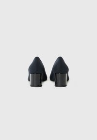 Navy high-heeled shoes with a chunky black heel, viewed from behind against a plain white background.