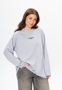 Lichtgrijze langemouwen shirt met de tekst "BOUNDARIES, BABE" in donkergroen. Zachte stof, relaxte pasvorm en brede mouwen. Casual en comfortabele stijl.