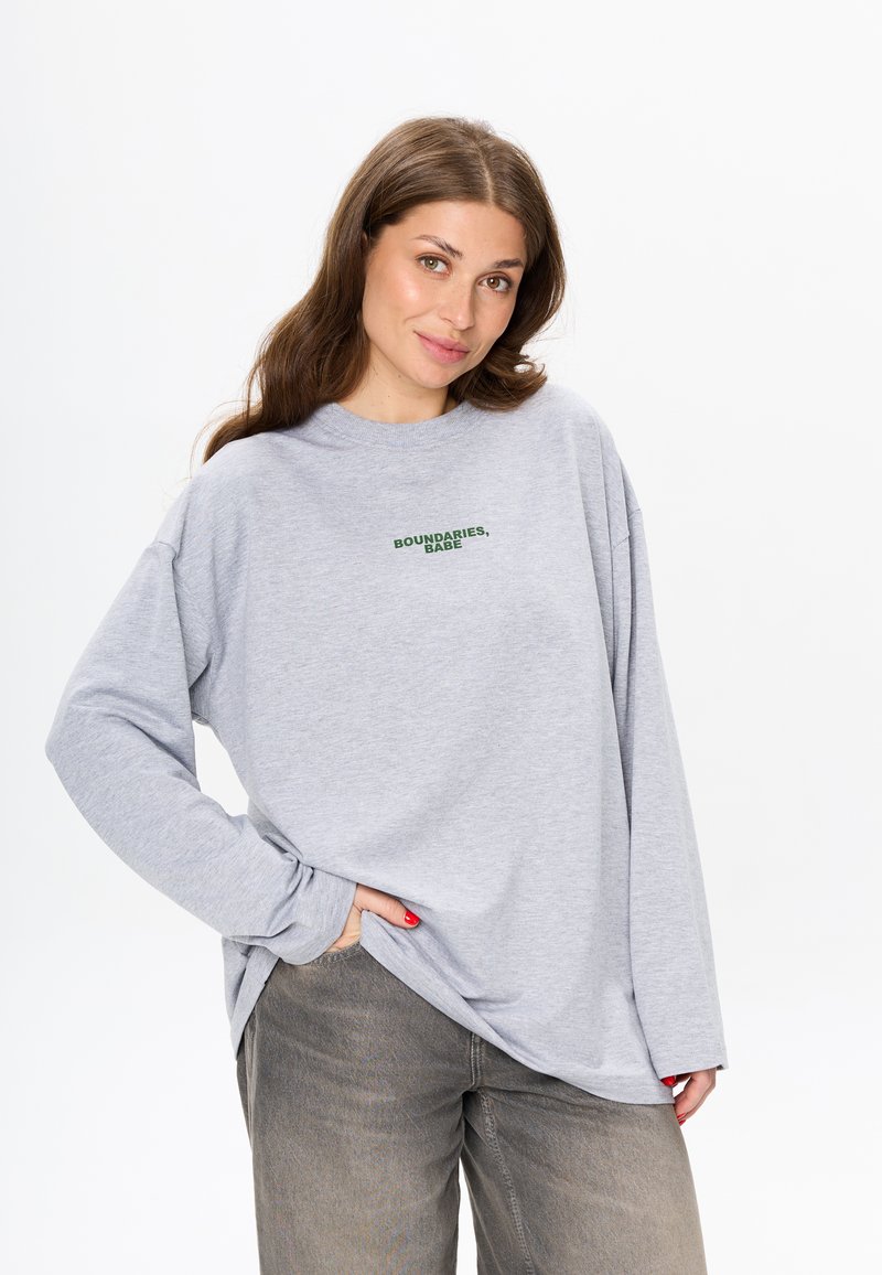 Lichtgrijze langemouwen shirt met de tekst "BOUNDARIES, BABE" in donkergroen. Zachte stof, relaxte pasvorm en brede mouwen. Casual en comfortabele stijl.