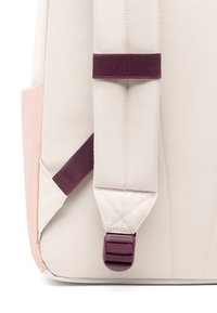 Batoh s béžovým hlavným telesom, ružovým akcentom a tmavočervenými popruhmi so sponou. Sú viditeľné textúrované tkaniny a detaily šitia.