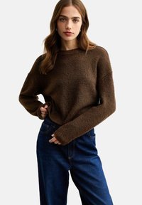 Maglione marrone a trama con scollo rotondo e maniche lunghe, abbinato a jeans in denim scuro a vita alta.
