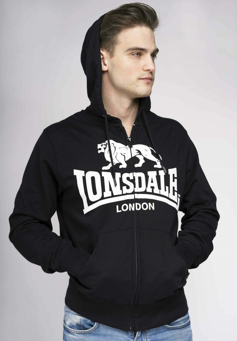Čierna mikina na zips vyrobená z bavlnenej zmesi, s bielym logom Lonsdale London, klokankovými vreckami a kapucňou so šnúrkou.