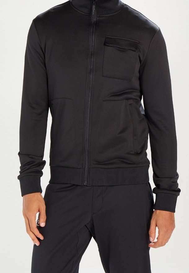 Schwarze Jacke mit Reißverschluss aus glattem Stoff. Verfügt über einen hohen Kragen, seitliche Taschen und eine Brusttasche mit Klappe. Figurbetonter Schnitt.
