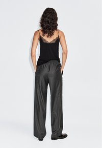 Zwarte cami-top met kantaccenten, gecombineerd met een grijze pantalon met wijde pijpen en een streepjesmotief. Beide items hebben een relaxte pasvorm en een zachte stof.