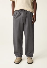 Graue Leinenhosen mit einem elastischen Bund und Kordelzug. Lockere Passform, Seitentaschen und schmal zulaufende Knöchel, kombiniert mit beigen Slippern.