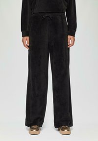 Zwarte corduroy wijde broek met een trekkoord in de taille, voorzien van een zachte textuur en zijzakken, gecombineerd met metallic sneakers.