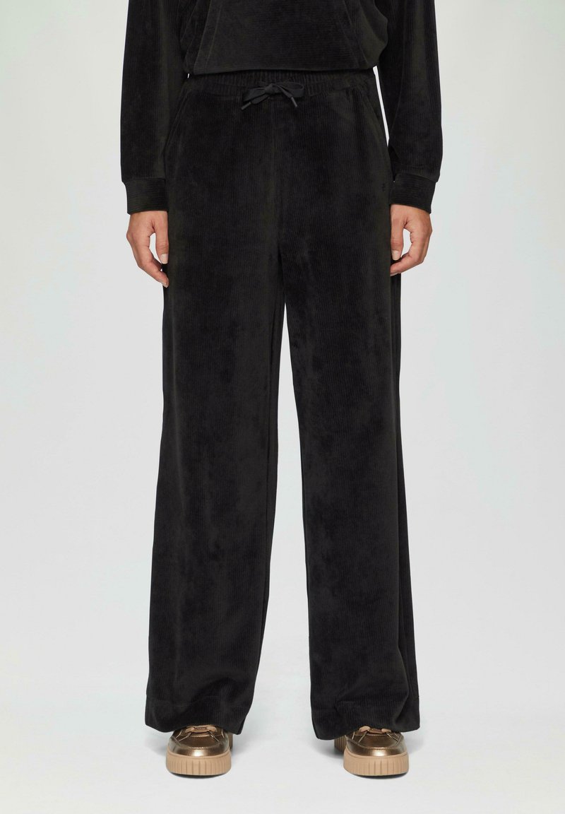 Zwarte corduroy wijde broek met een trekkoord in de taille, voorzien van een zachte textuur en zijzakken, gecombineerd met metallic sneakers.