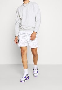 Sudadera gris, pantalones cortos blancos con contornos de hojas negras, calcetines blancos y zapatillas multicolores con acentos morados. Ropa urbana informal.