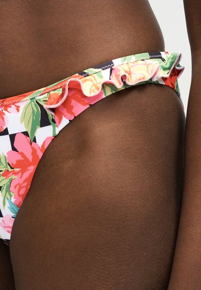 Κοντινό πλάνο ενός ατόμου που φοράει φλοράλ μπικίνι με βολάν, σε σκούρο δέρμα και απλό λευκό φόντο.