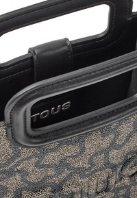 Bolso de mano con estampado en negro y beige, fabricado con tejido texturizado, acentos de cuero y dobles asas superiores. Presenta un logo plateado en el interior.