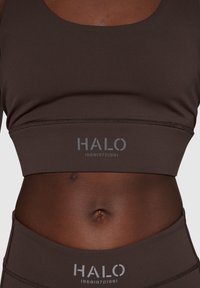 Brun atletisk crop top med rundad halsringning och logotryck "HALO" längs fållen. Slät tyg med en åtsittande design och matchande midjeresår.
