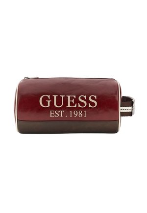 Trousse de toilette rectangulaire en cuir marron rouge et brun avec fermeture éclair, poignée latérale et inscription "GUESS EST. 1981" imprimée en blanc sur le devant.