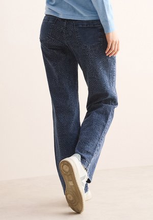 Donkerblauwe denim jeans met een textuurpatroon, rechte snit en zakdetails, gecombineerd met witte sneakers met een lichte accent.