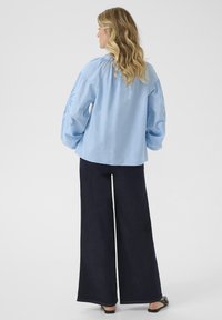 Camicia azzurro chiaro a maniche lunghe con maniche a sbuffo e dettagli ricamati. Indossata con pantaloni larghi in denim scuro, caratterizzati da un design semplice.
