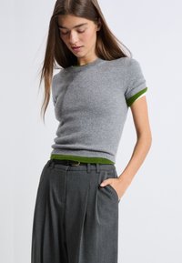 Szary dzianinowy sweter z zielonymi ściągaczami przy dekolcie i mankietach, zestawiony ze szarymi, dopasowanymi spodniami o plisowanym designie.