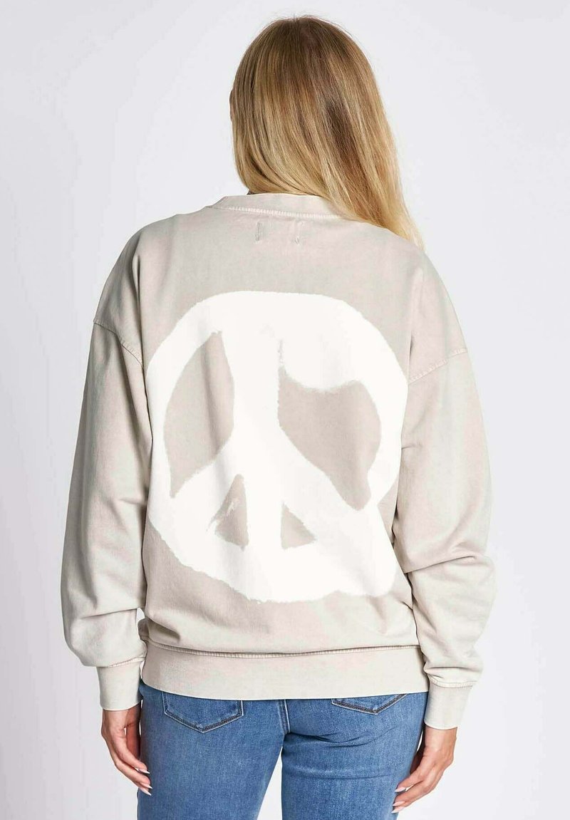 Beige Sweatshirt aus weichem Stoff mit einem großen weißen Friedenssymbol auf der Rückseite. Lockere Passform mit gerippten Bündchen und Saum.