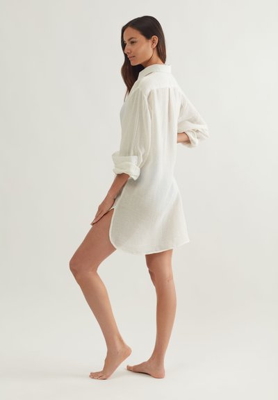 Λευκό, ελαφρύ φόρεμα πουκάμισο από υφασμά με υφή, με γιακά, μανσέτες με κουμπιά και στρογγυλεμένη εσοχή με πλαϊνές σκισμές για ευκολία στην κίνηση.