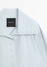 Camicia celeste chiaro con colletto, una fila di bottoni sul davanti e bottoni aggiuntivi sul bordo del colletto, etichetta con la scritta Massimo Dutti.