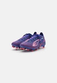 Lila och rosa fotbollsskor med en texturerad mesh-ovandel, snörning och röda dobbar för grepp på gräsytor.