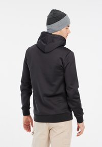 Zwarte hoodie met een zachte textuur, voorzien van een trekkoordkap en geribbelde manchetten. Gecombineerd met een grijze en zwarte muts.