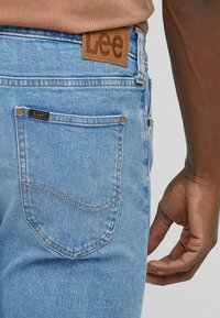 Jeans di denim azzurro chiaro con etichetta in pelle marrone con il logo "Lee", tasca posteriore con dettagli di cucitura e taglio aderente.