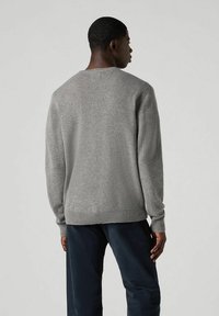 Szary sweter dzianinowy z okrągłym dekoltem, ściągaczami przy mankietach i u dołu. Miękka tekstura, dopasowany fason, widok z tyłu na neutralnym tle.